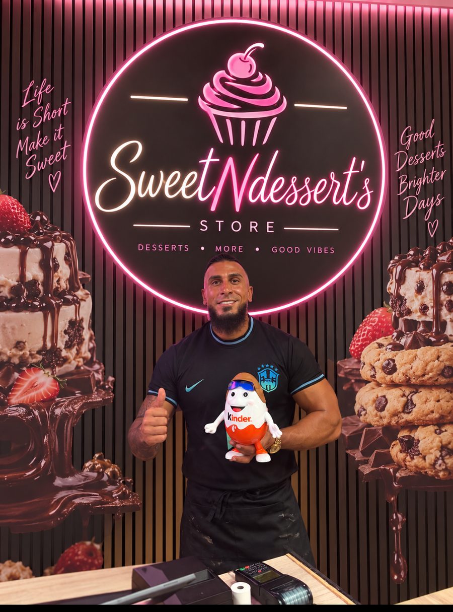 Walid i butikken foran neonskiltet med maskotten Miklo i hånden
